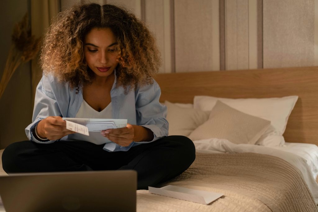 Thoughtful woman sitting on her bed reviewing financial documents, reflecting on personal planning and the impact of spousal support decisions.