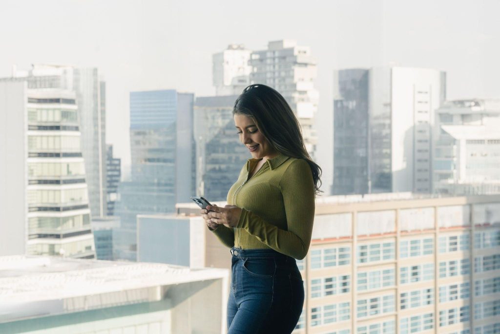Professional woman using smartphone for electronic faxing in modern high-rise office with cityscape view.